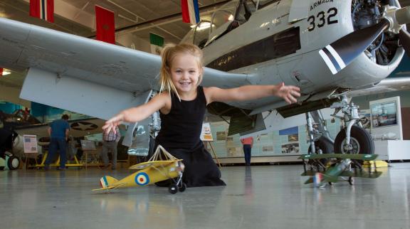 A young girl pushes toy planes in front of a full sized one on display
