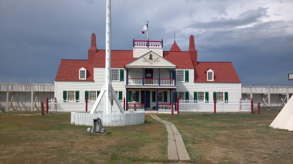 A large, historic building with a red roof and white exterior, featuring a central flagpole in front
