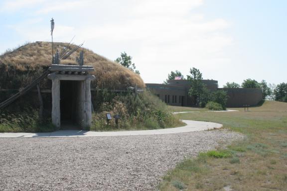 An earth lodge structure at a historical site, with a grassy roof and a pathway leading to its entrance