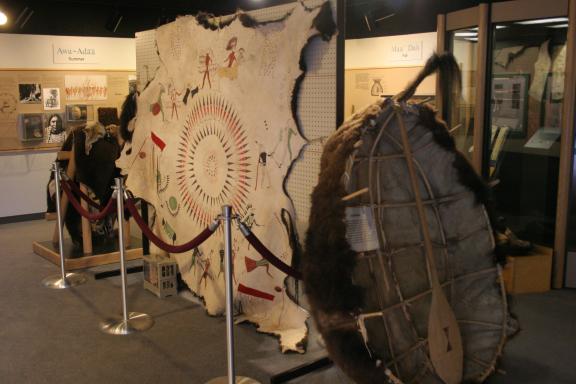 A museum display featuring a large, decorated hide with indigenous artwork, surrounded by various artifacts and traditional items