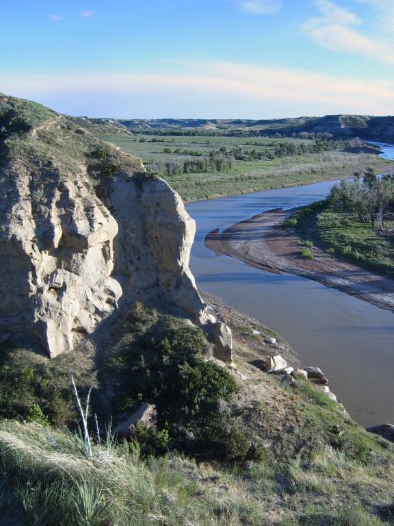 A scenic view of the Badlands with a winding river flowing through a landscape of rugged cliffs and green hills