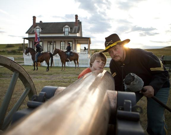A man wearing a cowboy hat is loading a cannon, with a boy standing beside him