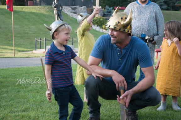 A man wearing a Viking helmet, kneeling with a child