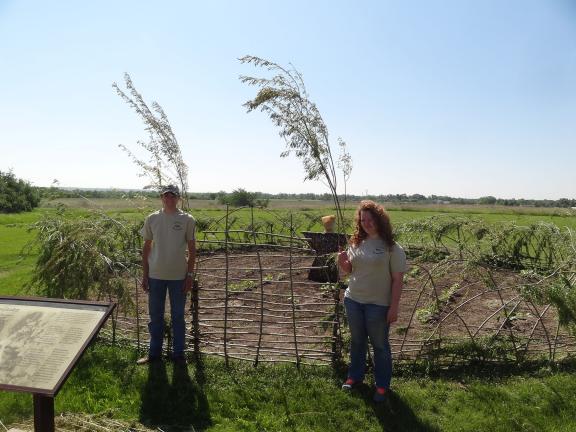 Two people are standing near a reconstructed garden plot, bordered by a wooden fence