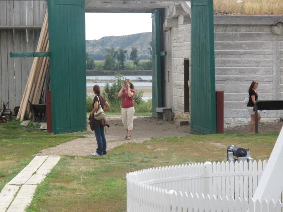 People walking through a large wooden gate of a historic fort or settlement