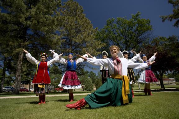 A wide view of a cultural dance, capturing the entire group of dancers in traditional costumes performing on an outdoor setting