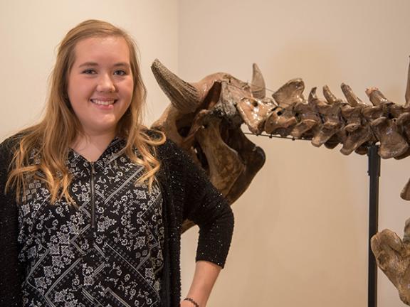 Jennifer Nannega smiling and standing next to a large fossil display