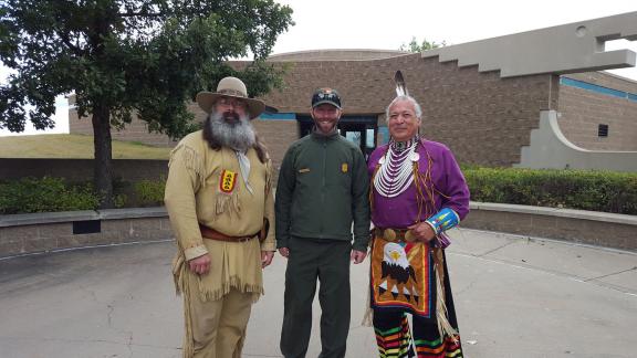 Three individuals dressed in period clothing are standing together outdoors