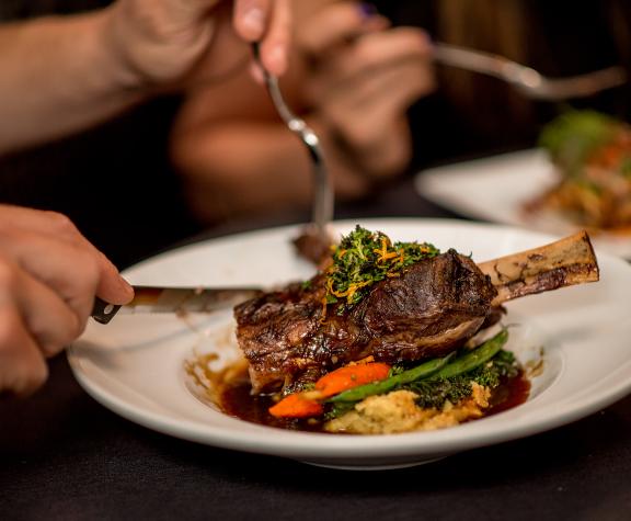 A close-up of a plated meal, featuring a perfectly cooked steak garnished with herbs, served on a bed of vegetables and a rich sauce
