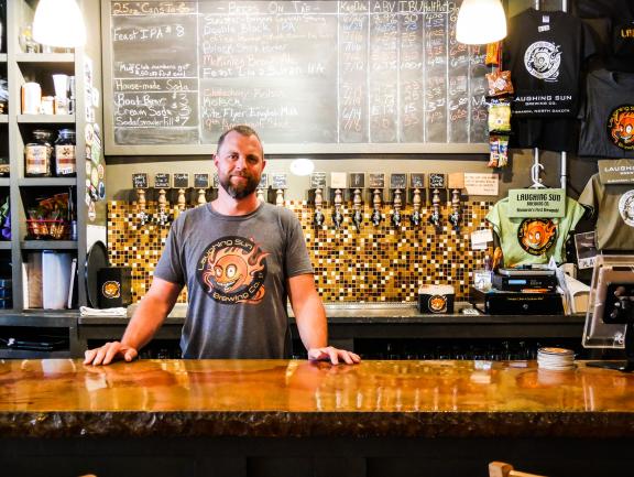 Mike Frohlich stands behind a wooden bar counter in a bar