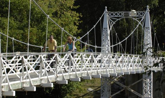 A suspension bridge spans over a river, with cyclists crossing it