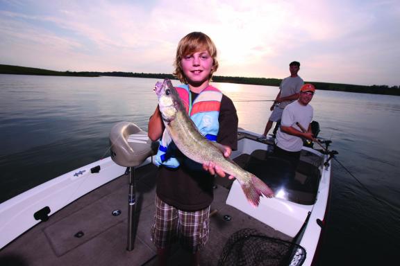 A person proudly holding a large fish while standing on a boat, with another person