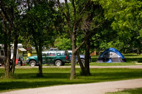 Several RVs are parked in a green, wooded area, suggesting a campground