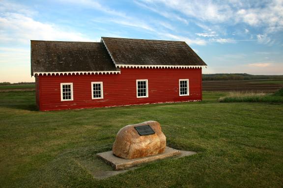 A red wooden building with a gabled roof stands on a well-kept lawn