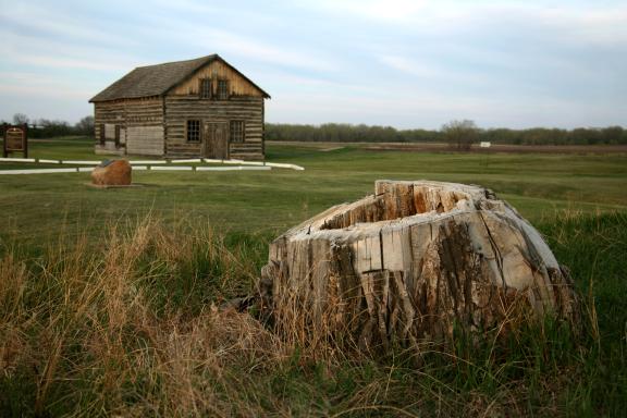 An old stone well sits in the foreground with a rustic log cabin