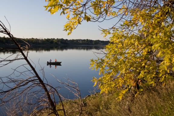A boat with people fishing is visible on a calm lake, framed by trees