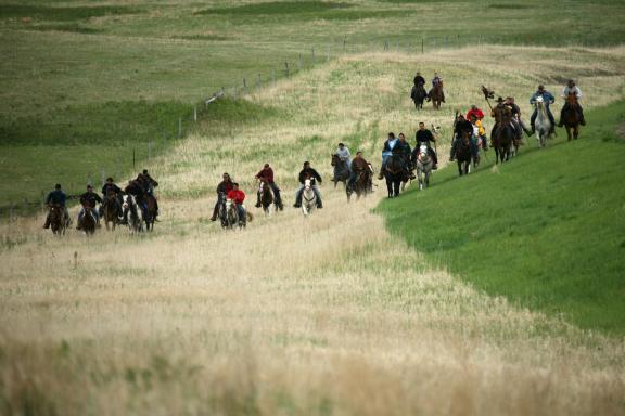 A group of people riding horses across open grasslands, moving along a winding path