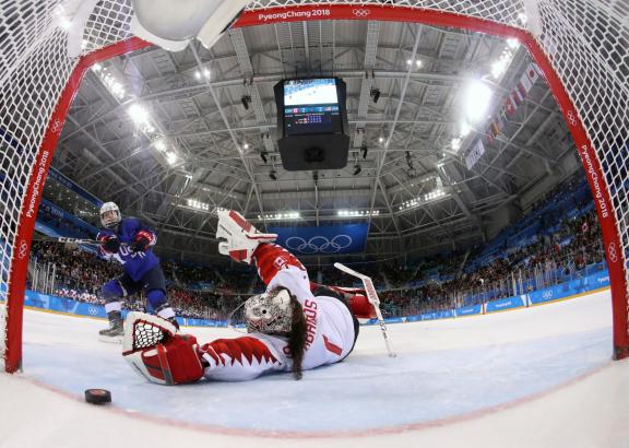 A fisheye view of a hockey goalie on the ice in front of the net, with a player nearby 