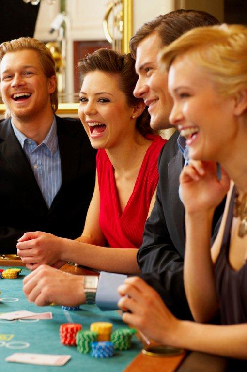 A group of people dressed in formal attire are gathered around a casino table, smiling and laughing