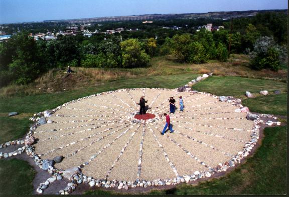 Several people are standing and walking around a a medicine wheel