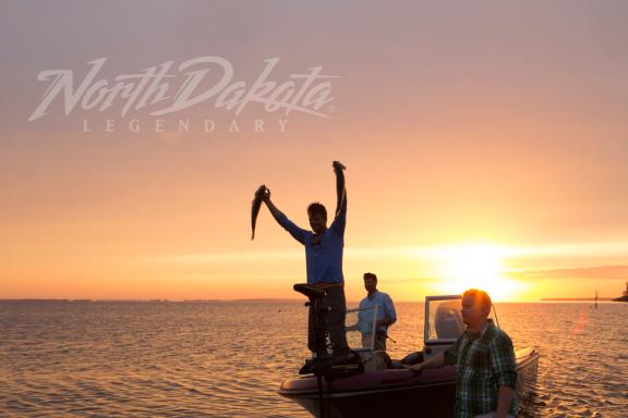 Two people fishing from a boat during sunset