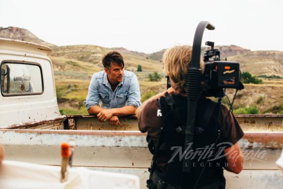 A man leaning on the back of a truck, being filmed 
