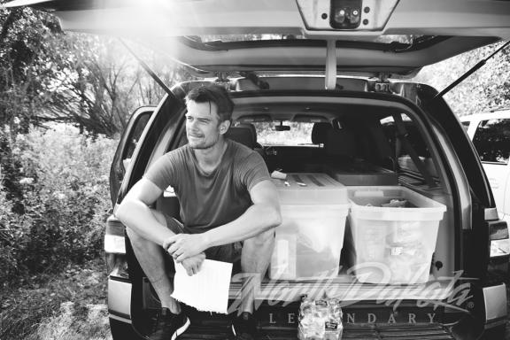 A person sitting on the back of a car, with the trunk open