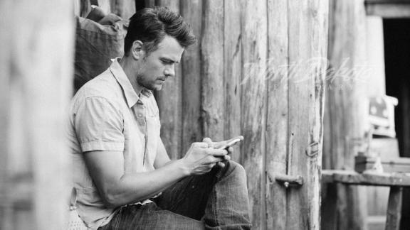 A man seated, using a smartphone, in a rustic setting