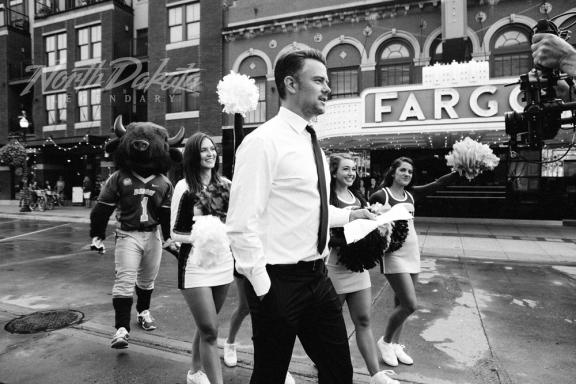 A man in a suit walking with a group of cheerleaders