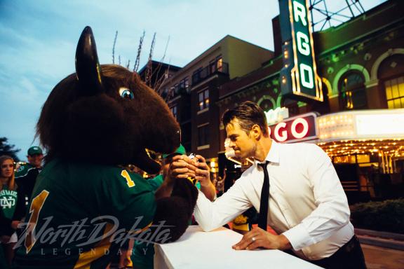 Man in a suit interacting with a large animal mascot