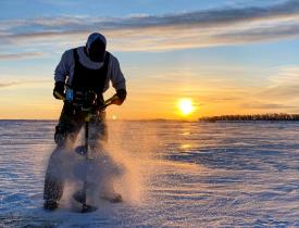 Man drilling hole at sunrise for ice fishing