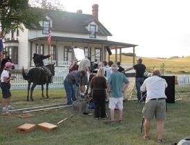A film crew surrounds the talent on the grounds at Fort Abraham Lincoln.